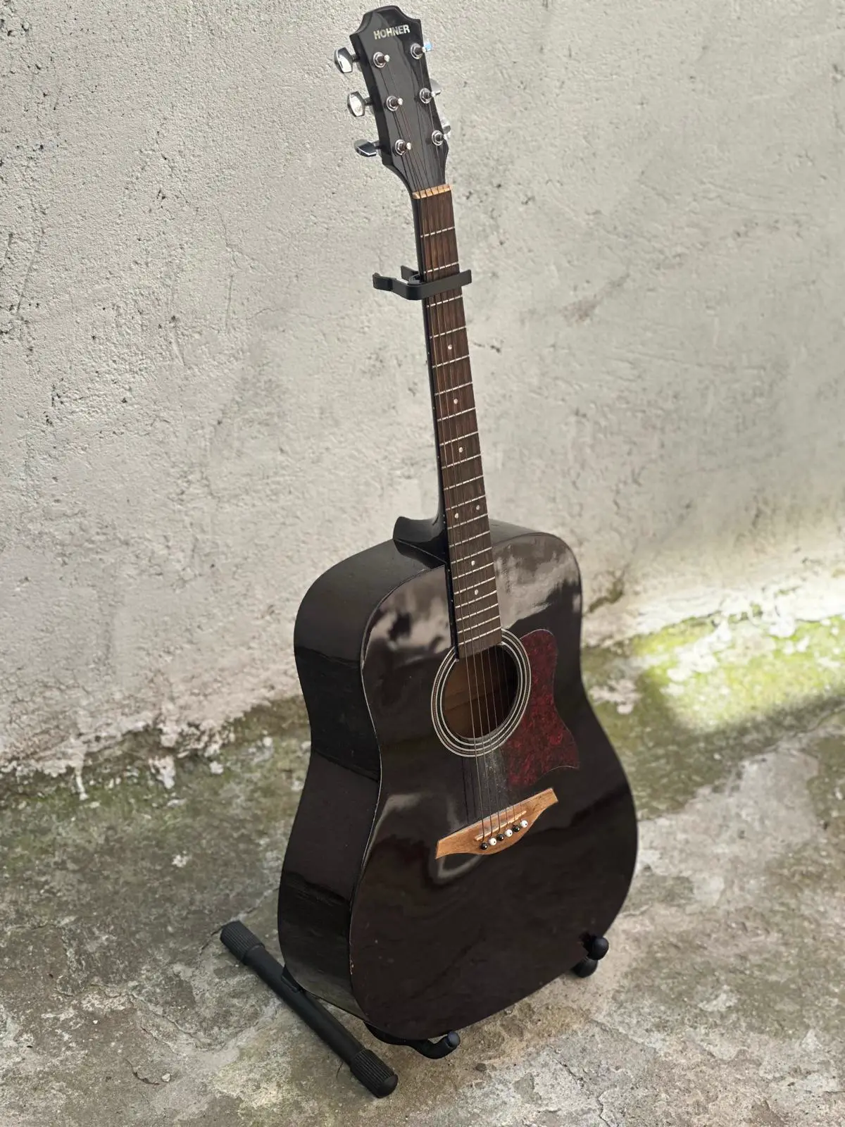 Andrei's black Hohner guitar on a stand by a concrete wall.