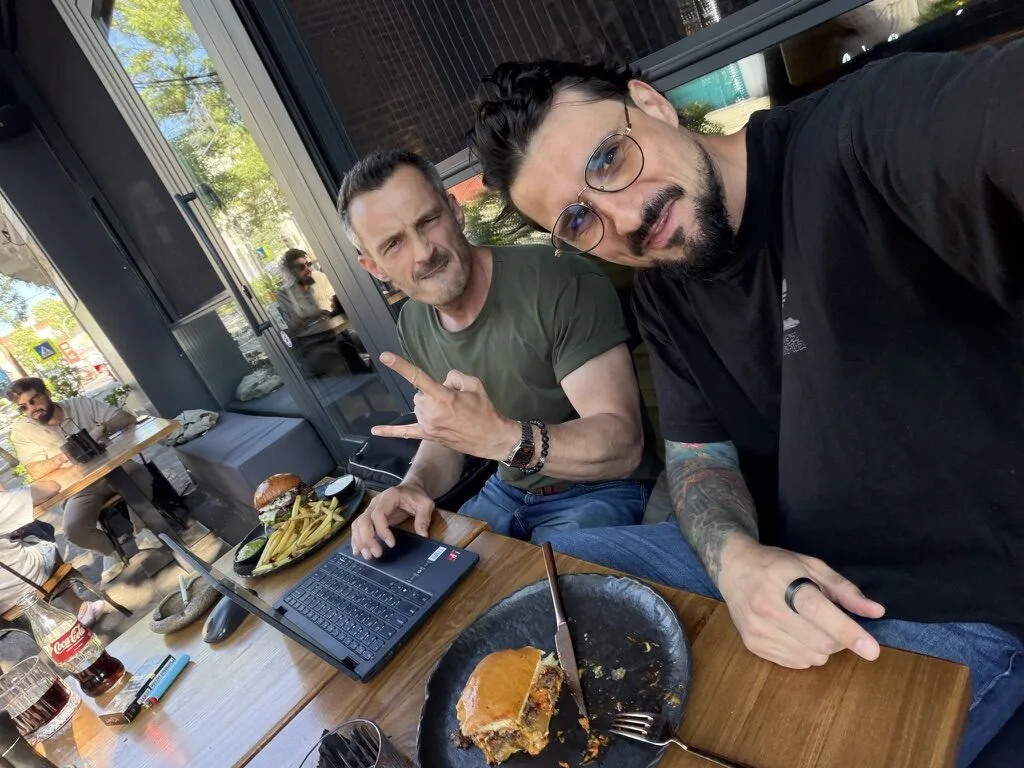 Andrei and Radu at a table, laptop open between the plates – a working session.